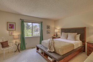 A bedroom with a bed, bedside tables, a bench, a window with curtains, and framed pictures on the wall. - Tubing Promo! Bright Uptown Condo w/ Cozy Fireplace, Large Deck, Mountain Views, Walk to Amenities (Pagosa Springs)