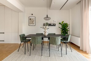 A modern dining area with a dark wooden table, green upholstered chairs, a white vase centerpiece, and a hanging pendant light.