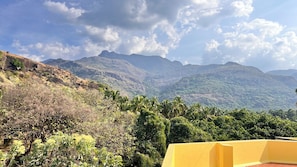 A mountainous landscape with a view of distant peaks and a yellow building in the foreground. - MM Garden (Tarangambadi)