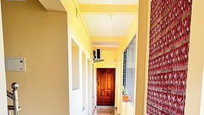 Ein Korridor mit gefliestem Boden, einer Holztür am Ende und einer roten Wand rechts.
