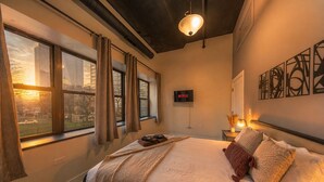 Une chambre à coucher avec un lit, un téléviseur et une vue sur le paysage urbain grâce à de grandes fenêtres.