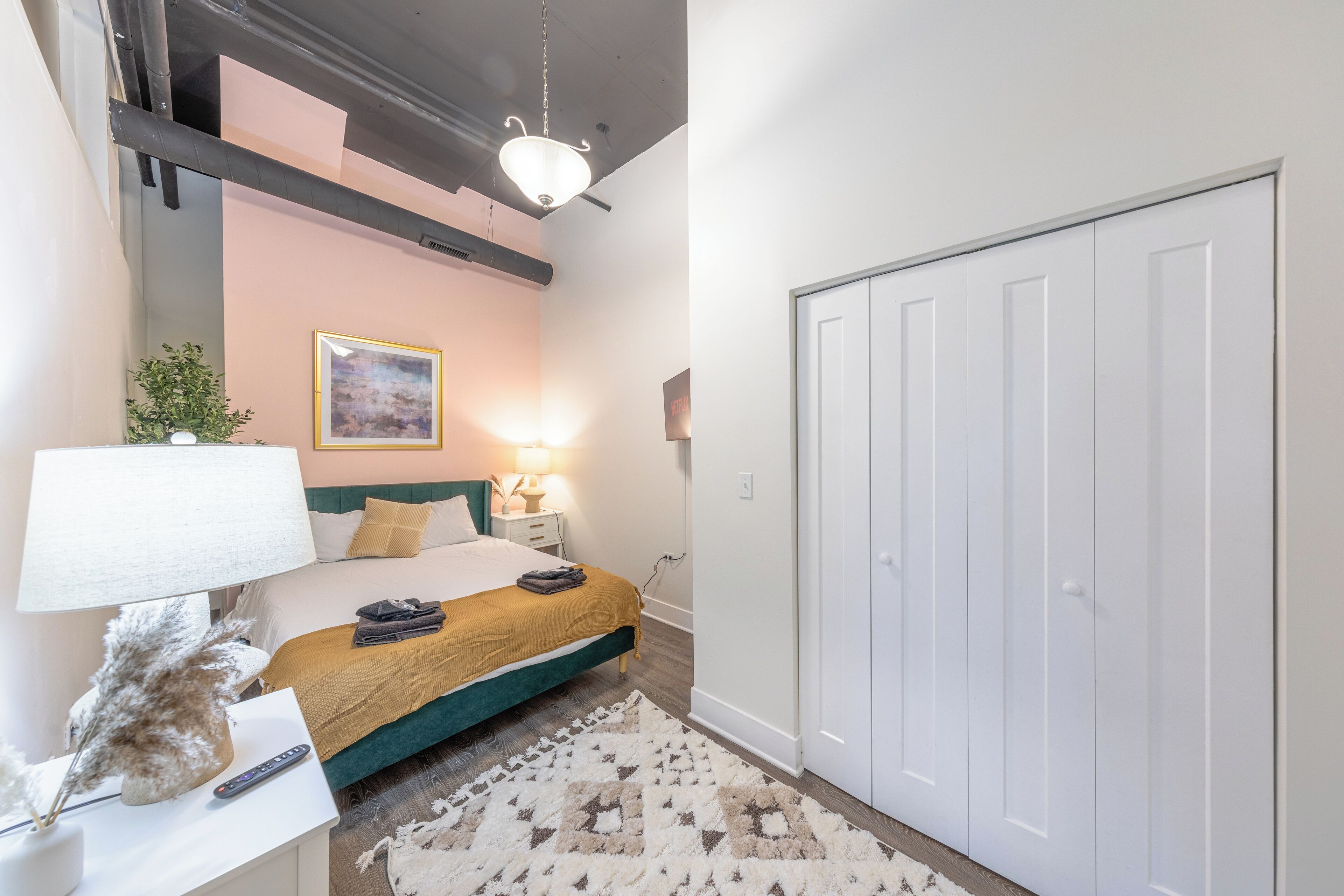 Quarto com cama, mesa de cabeceira, abajur e guarda-roupa.