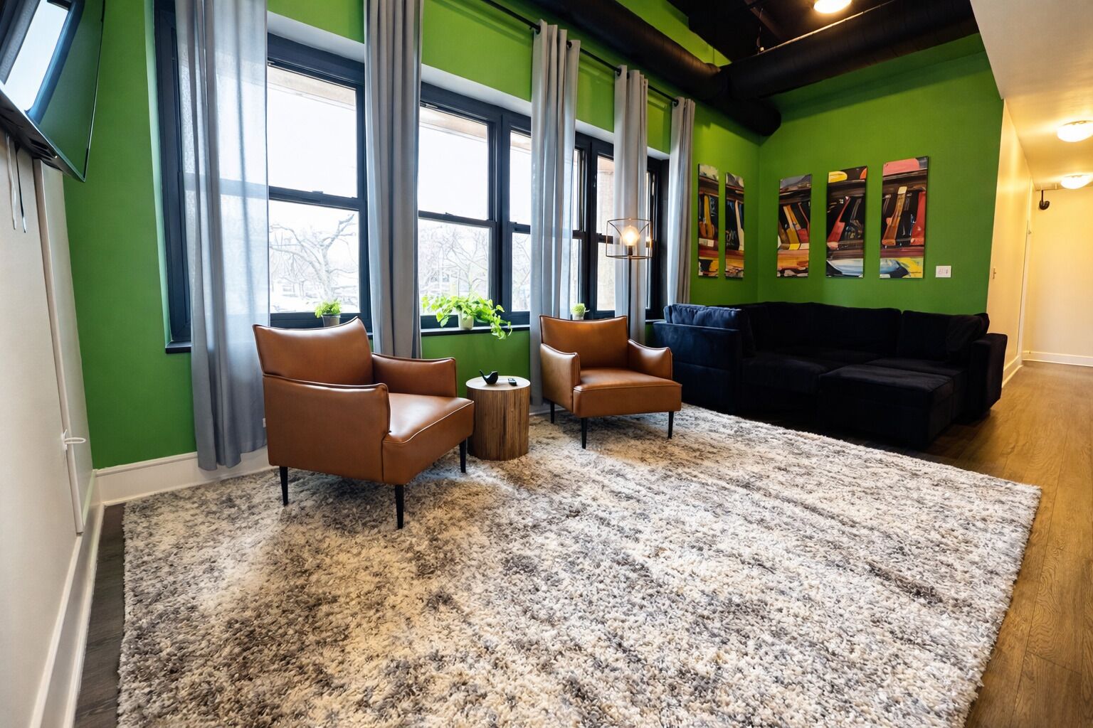 Un salon moderne avec des murs verts, de grandes fenêtres et un canapé noir.
