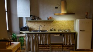 A compact kitchen with a sink, stove, and white refrigerator. There is a wooden table and chairs, and a window providing natural light.
