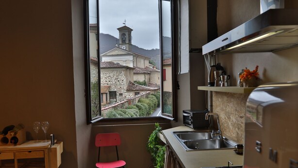 A kitchen with a view of a church and mountains, a red chair, a sink, and a stove.