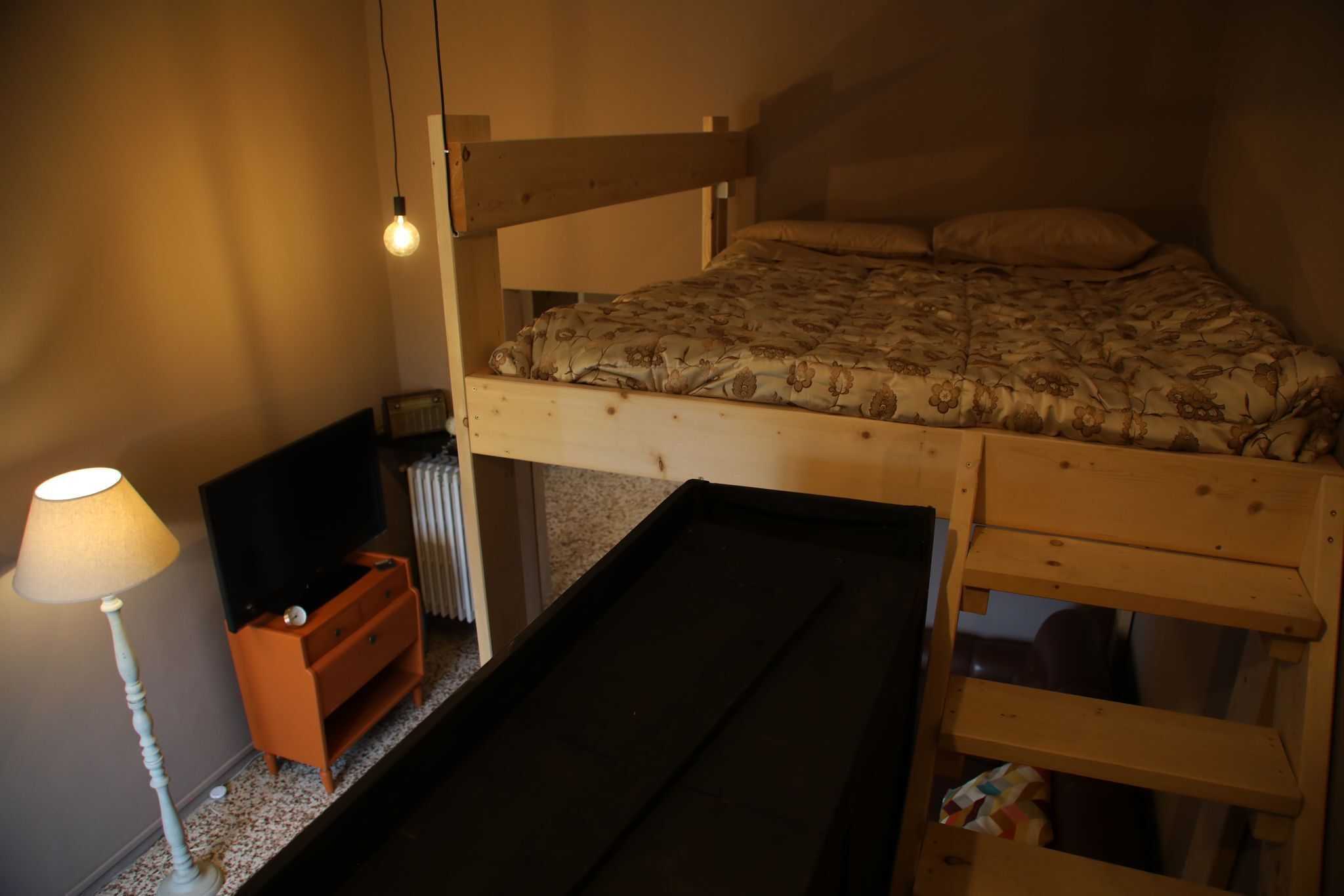 A bunk bed with a wooden frame, a TV on a dresser, a lamp, and a radiator.