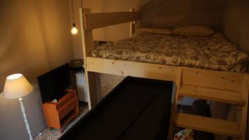 A bunk bed with a wooden frame, a TV on a dresser, a lamp, and a radiator.