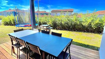 Un patio exterior con mesa y sillas, un trampolín y vistas a casas y vegetación.