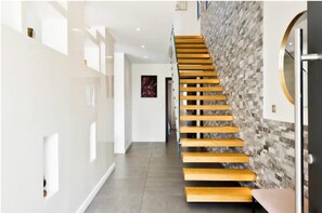 A modern interior with a wooden staircase, white walls, and a textured wall on the right.