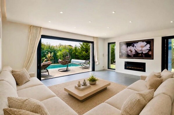 A modern living room with a large sofa, a coffee table, and a flat-screen TV mounted on the wall.