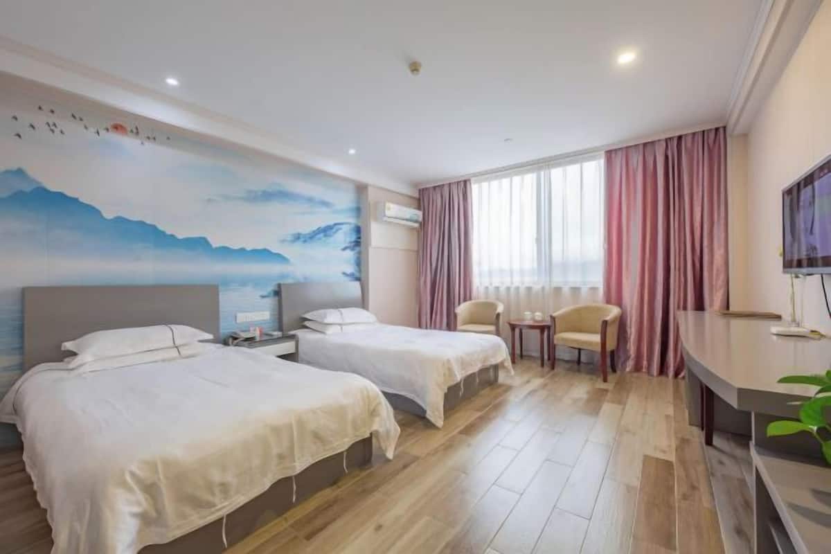 A hotel room with two beds, a desk, a chair, a TV, and a mural on the wall.