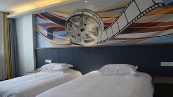 A hotel room with two beds, a large film reel mural on the wall, and a modern headboard.