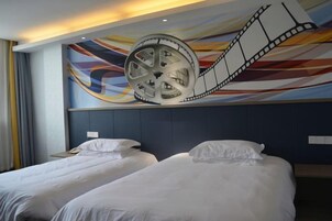 A hotel room with two beds, a large film reel mural on the wall, and a modern headboard.
