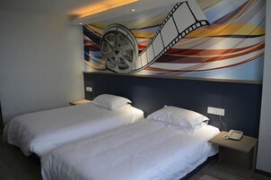 Habitación de hotel con dos camas, un mural en la pared con carrete y película, y un teléfono en la mesita de noche.