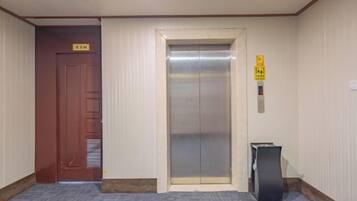 A hotel elevator with a sign above it, a wooden door to the left, and a trash bin to the right.