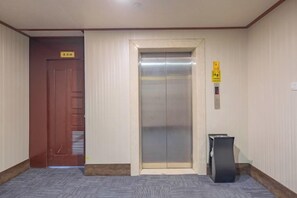A hotel elevator with a sign above it, a wooden door to the left, and a trash bin to the right. - Hong Xiang Hotel (Xiangshan)