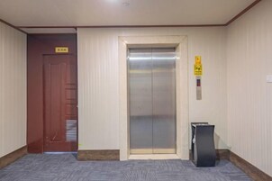 A hotel elevator with a sign above it, a wooden door to the left, and a trash bin to the right.