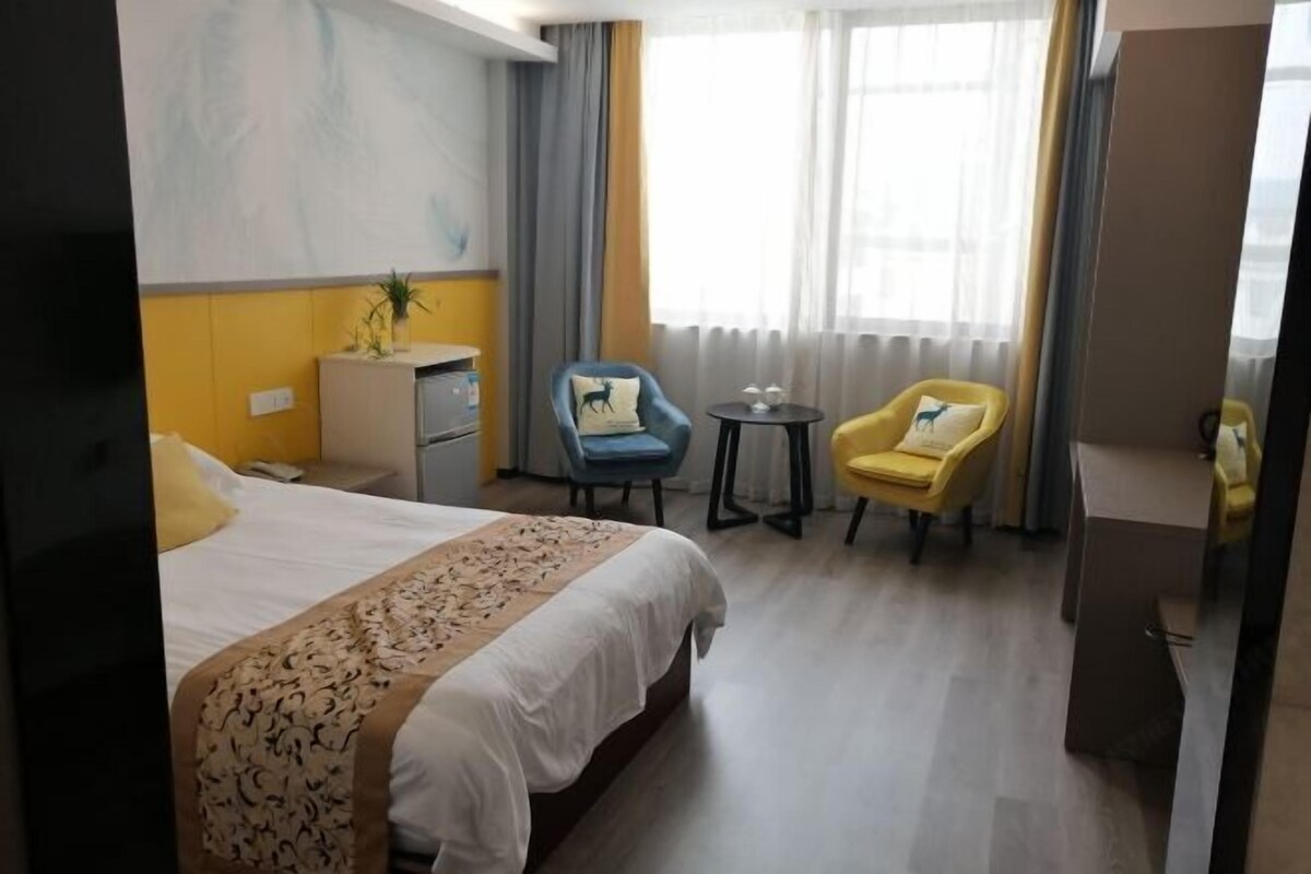 A hotel room with a bed, a desk, two chairs, a small table, and a large window with curtains.