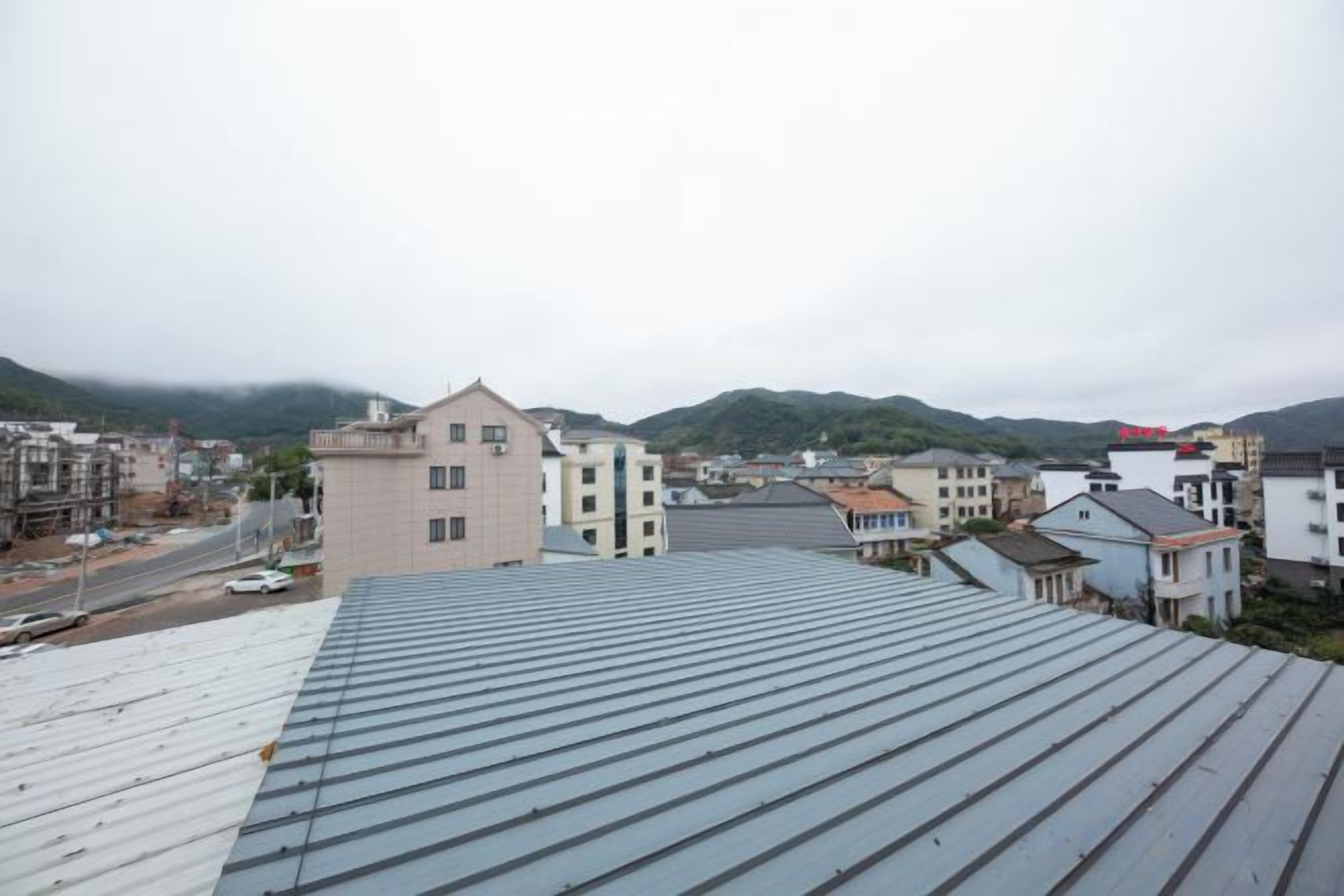 A residential area with buildings, a road, and a hilly landscape in the background.