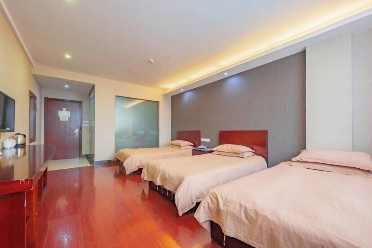 A hotel room with three beds, wooden flooring, a TV, and a desk.