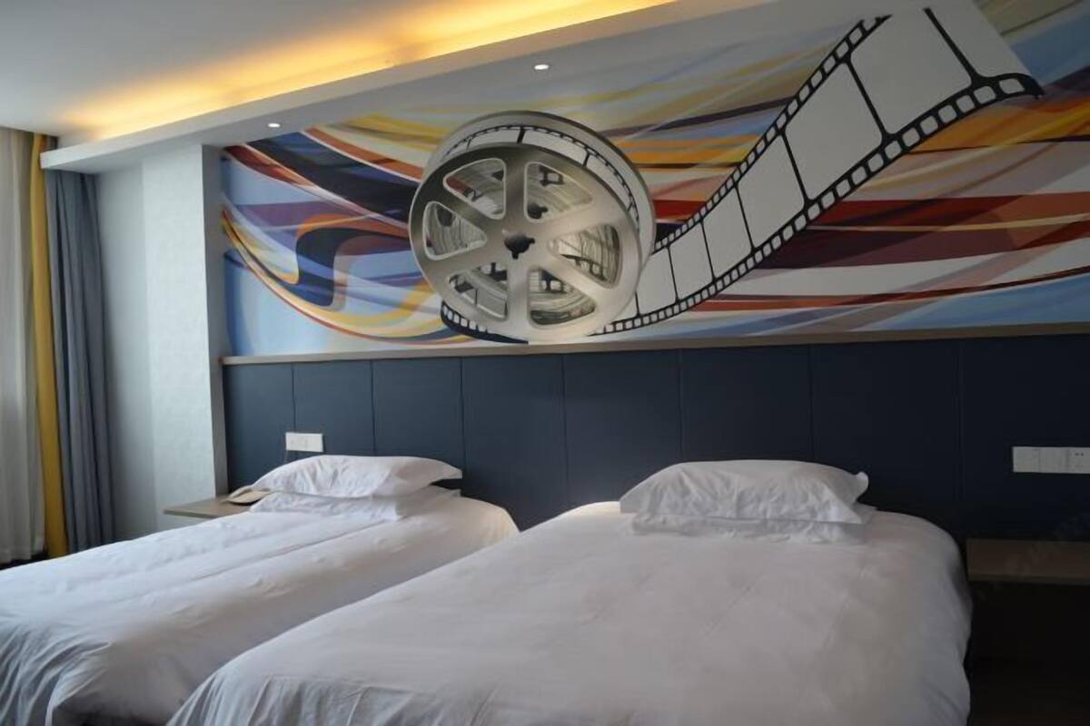 A hotel room with two beds, a large film reel mural on the wall, and a modern headboard.