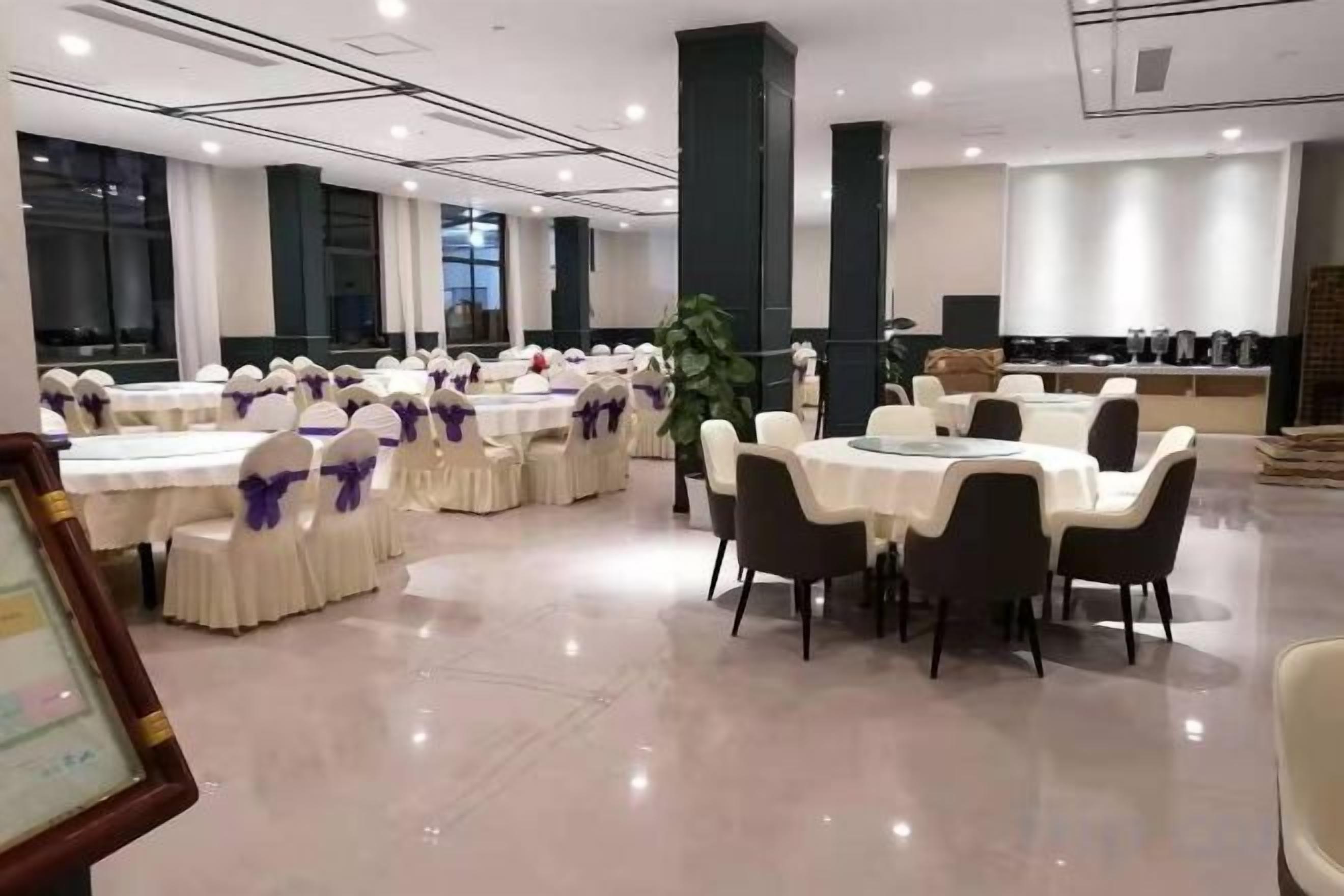 Une salle de banquet avec des tables et des chaises rondes, une scène et un espace cuisine.