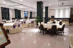 Un salón de banquetes con mesas y sillas redondas, un escenario y una zona de cocina.