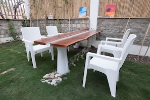 A wooden table with white chairs in a grassy outdoor area.