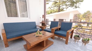 Un área de estar moderna al aire libre con una mesa de madera y sillas azules con cojines, una pequeña mesita de madera con un farol, y cestas de mimbre con plantas.
