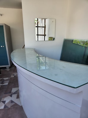 A reception desk with a glass top, a wall-mounted mirror, and a tiled floor.