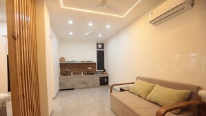Una sala de estar moderna con un sofá, un separador de madera y una zona de cocina al fondo.