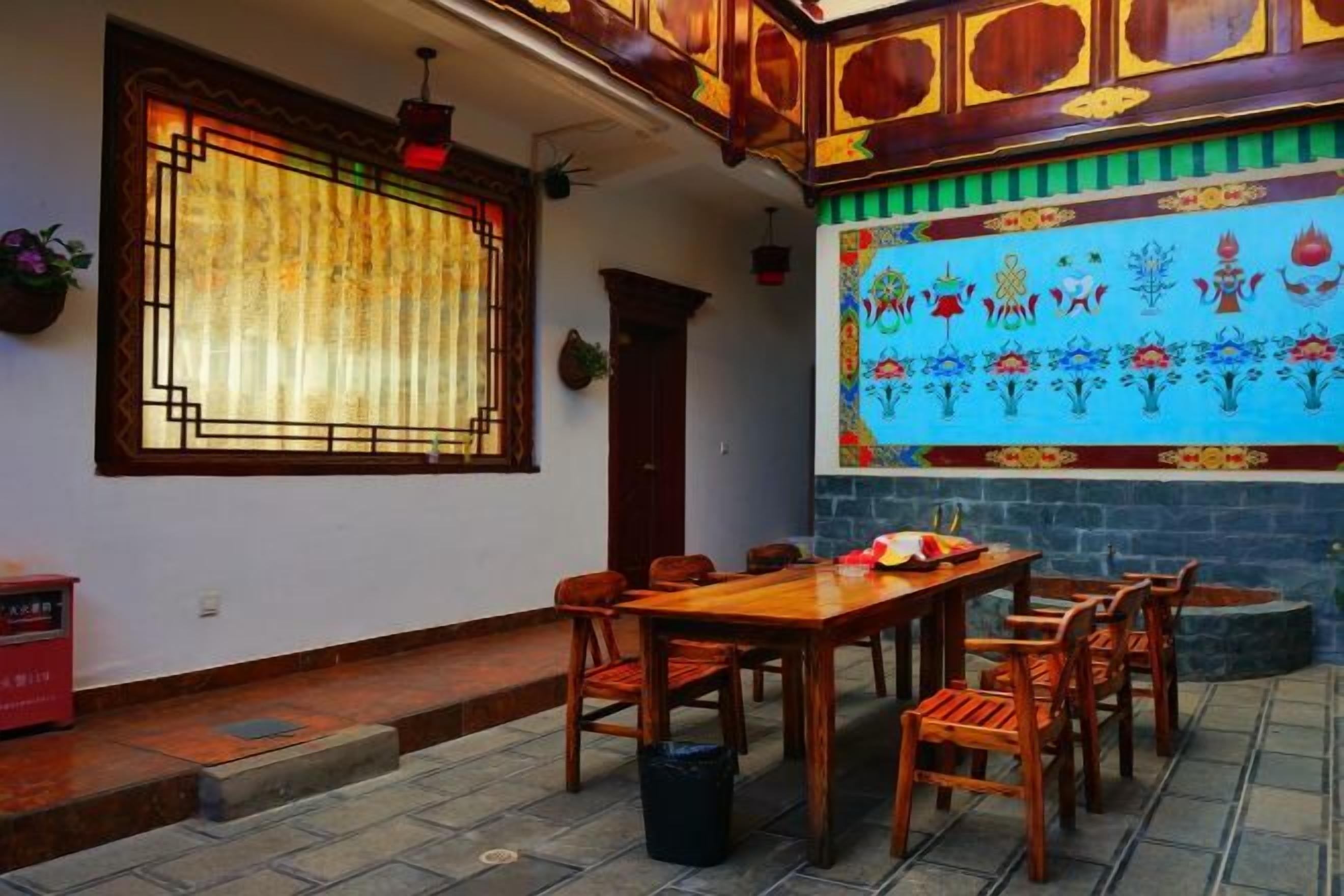 A traditional room with a dining table and chairs, a window with a curtain, and a colorful wall mural.