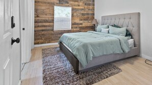 A bedroom with a bed, a window, a wooden wall, and a door. - 4BR Charming Home By Beachside (West Palm Beach)