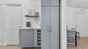 A compact kitchen with grey cabinets, a small fridge, and a dining area with a table and chairs. - 4BR Charming Home By Beachside (West Palm Beach)