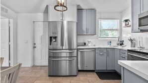 A modern kitchen with stainless steel appliances, grey cabinetry, and a herringbone wood floor. - 4BR Charming Home By Beachside (West Palm Beach)