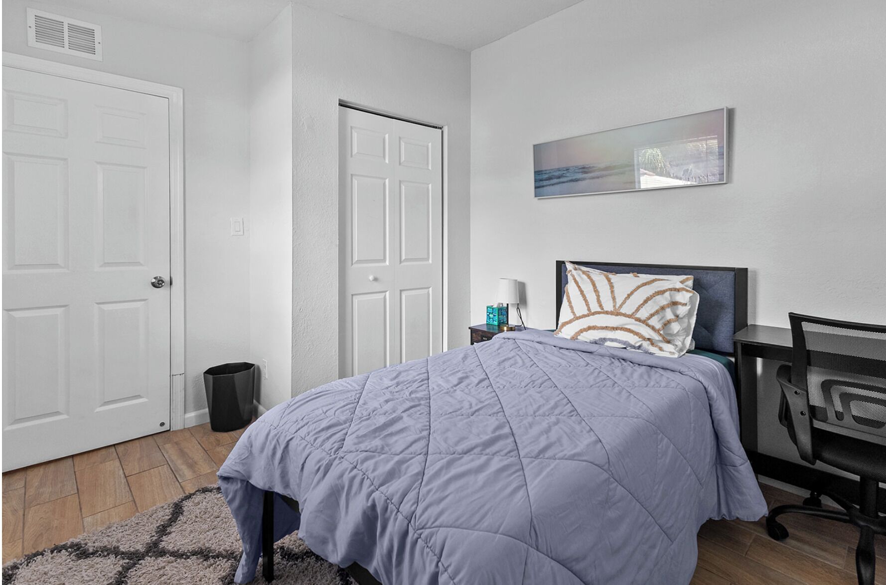Ein Schlafzimmer mit Bett, Nachttisch, Stuhl, Wandbild und einer Tür.