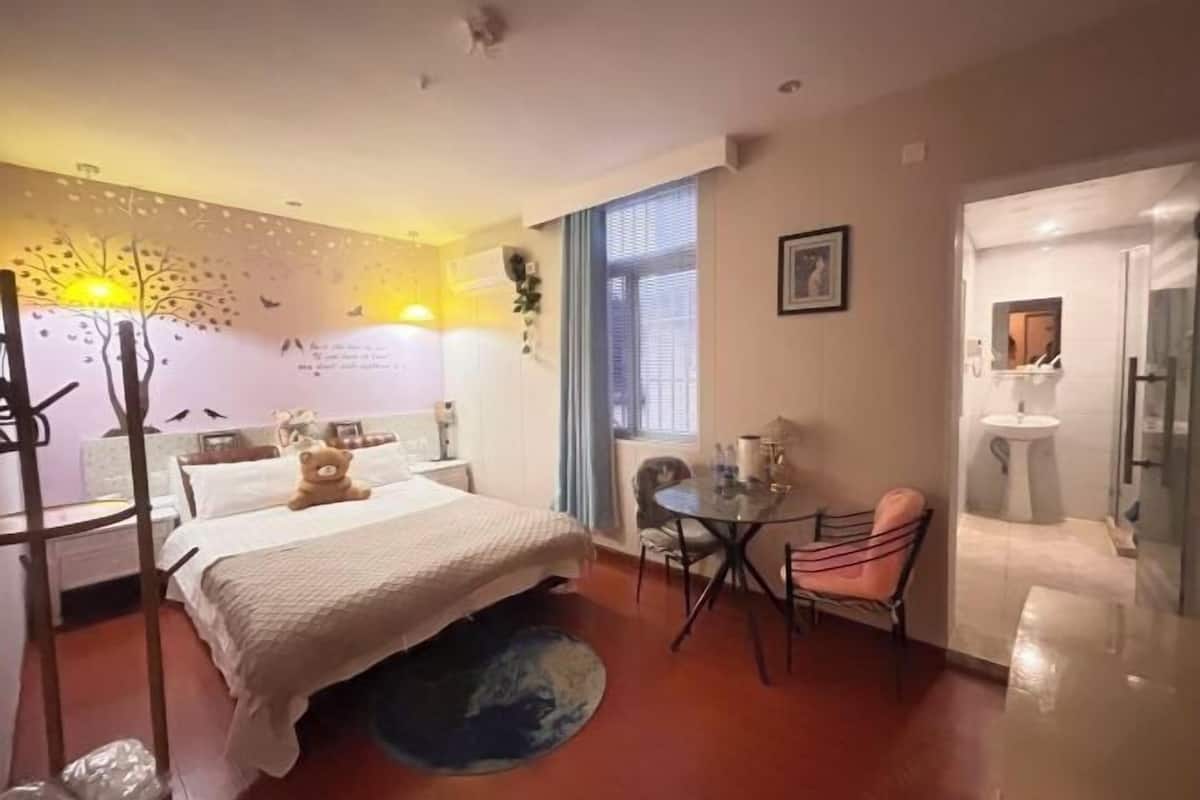 Ein Hotelzimmer mit einem Bett, einem runden Tisch, einem Stuhl, einem kleinen Fenster und einem durchgegangene Tür erkennbaren Badezimmer.