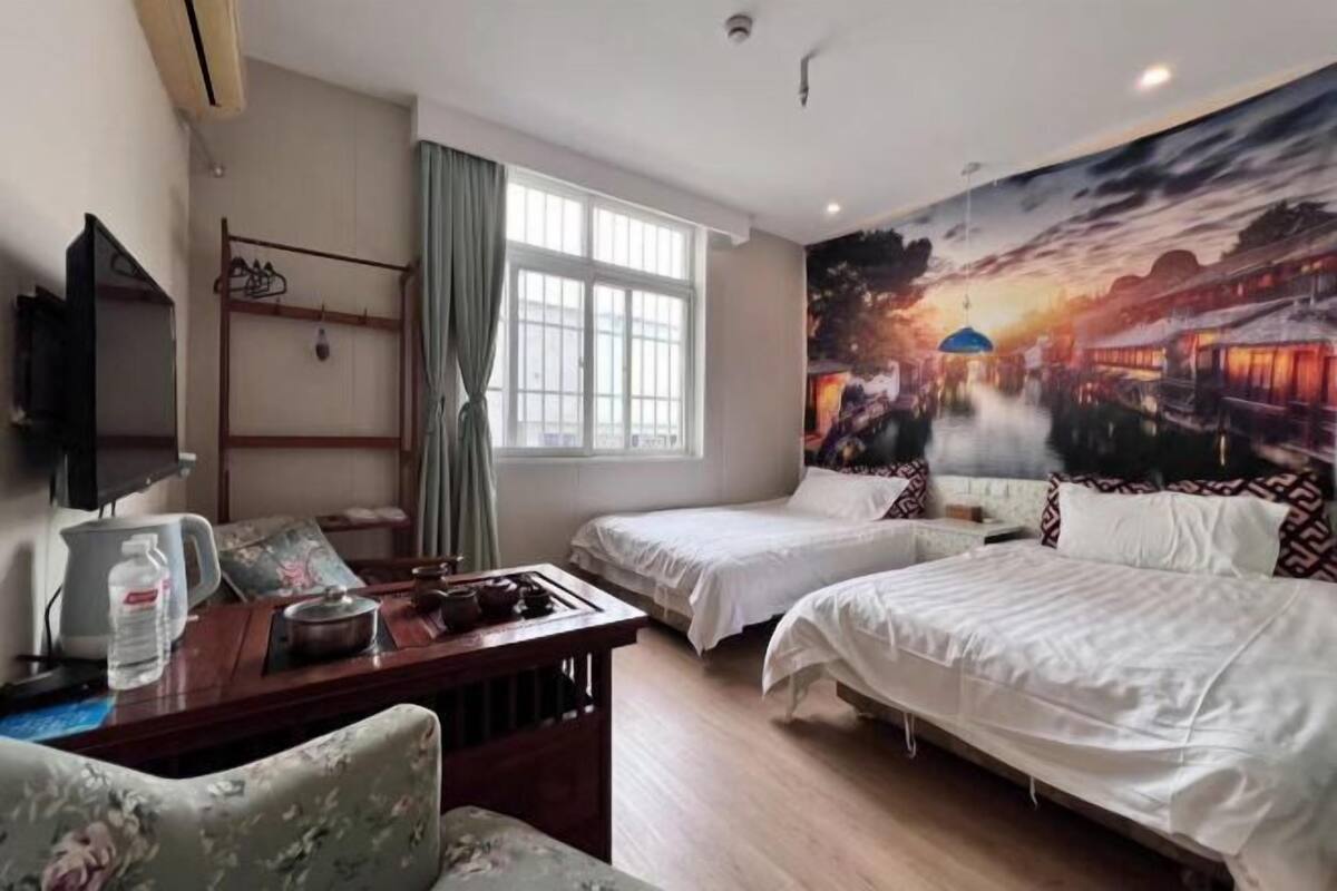 Ein Hotelzimmer mit zwei Betten, einem Schreibtisch mit Stuhl, einem Fernseher und einem großen Fenster.