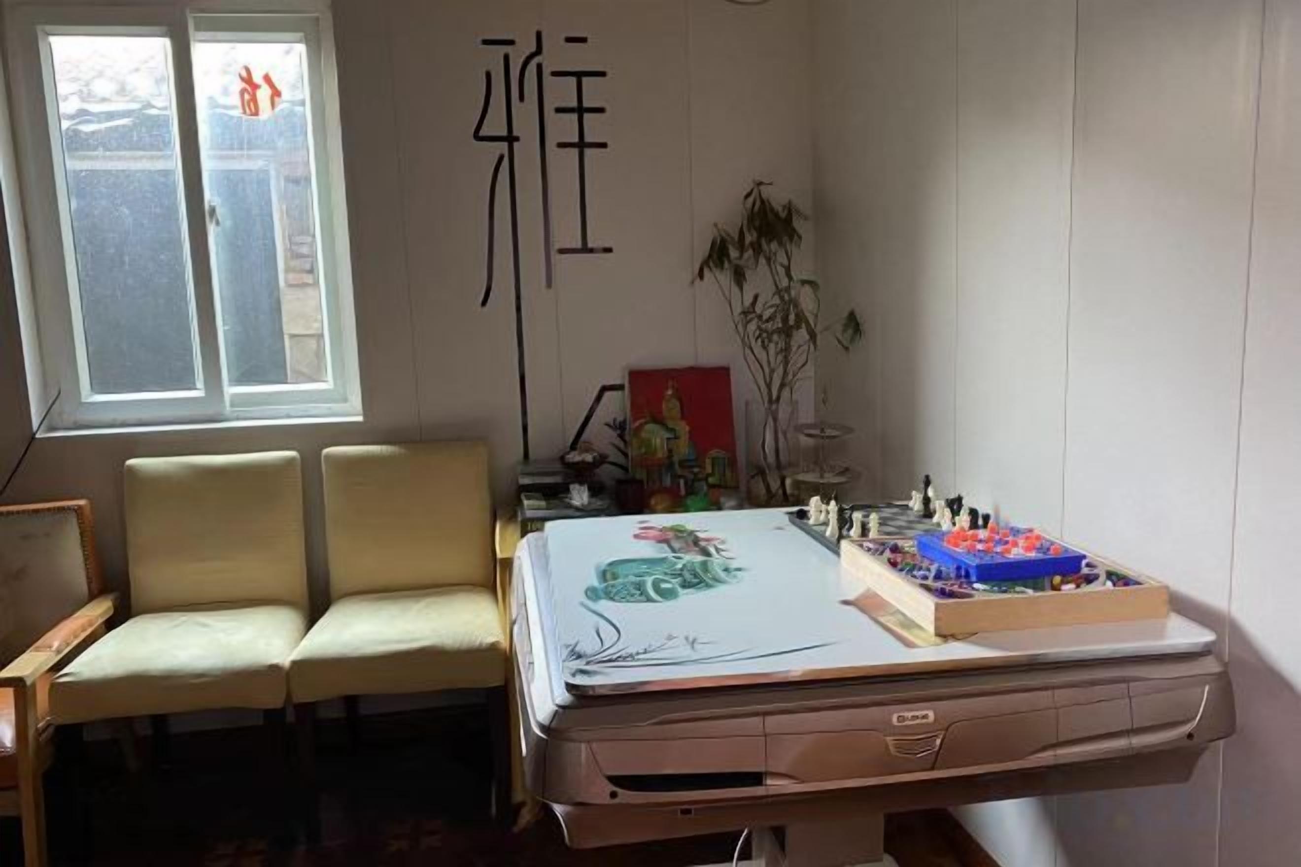 A room with a desk, two chairs, a window, and a decorative item on the wall.