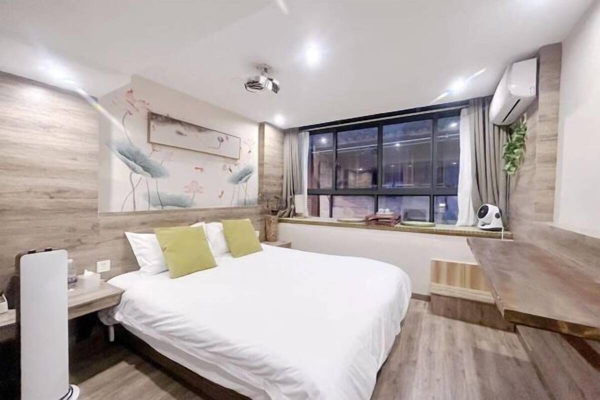 Ein Hotelzimmer mit Bett, Nachttisch, Fenster und Wandbildern.
