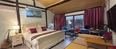 A bedroom with a bed, bedside table, lamp, and a guitar. There is a dining area with a table and chairs.