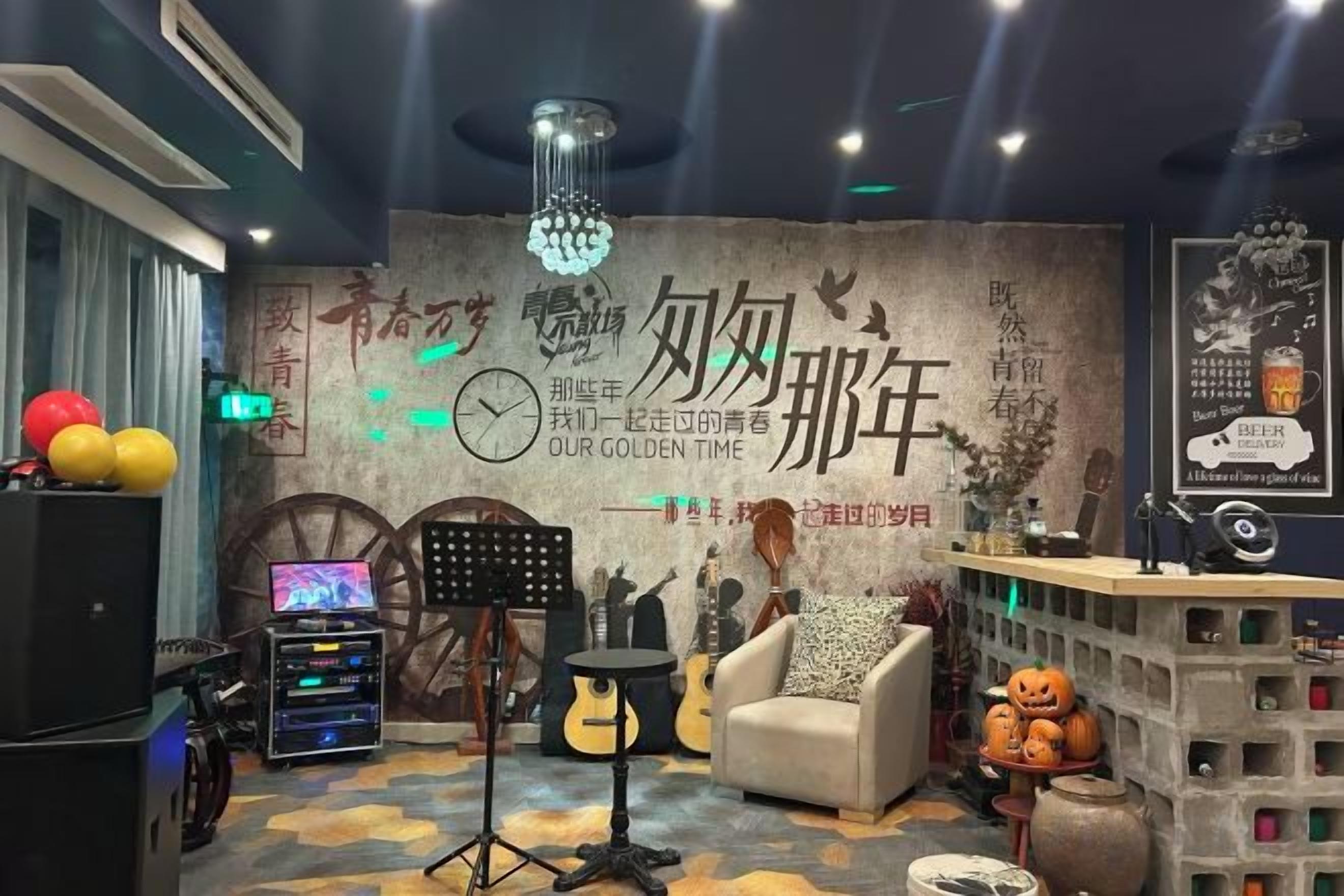 A room with a piano, a sofa, a table with a lamp, and a decorative wall with text and a clock.