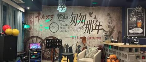 A room with a piano, a sofa, a table with a lamp, and a decorative wall with text and a clock.