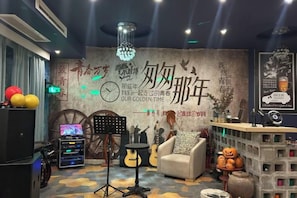 Une pièce comprenant un piano, un canapé, une table avec une lampe, et un mur décoratif orné de motifs et d’une horloge.