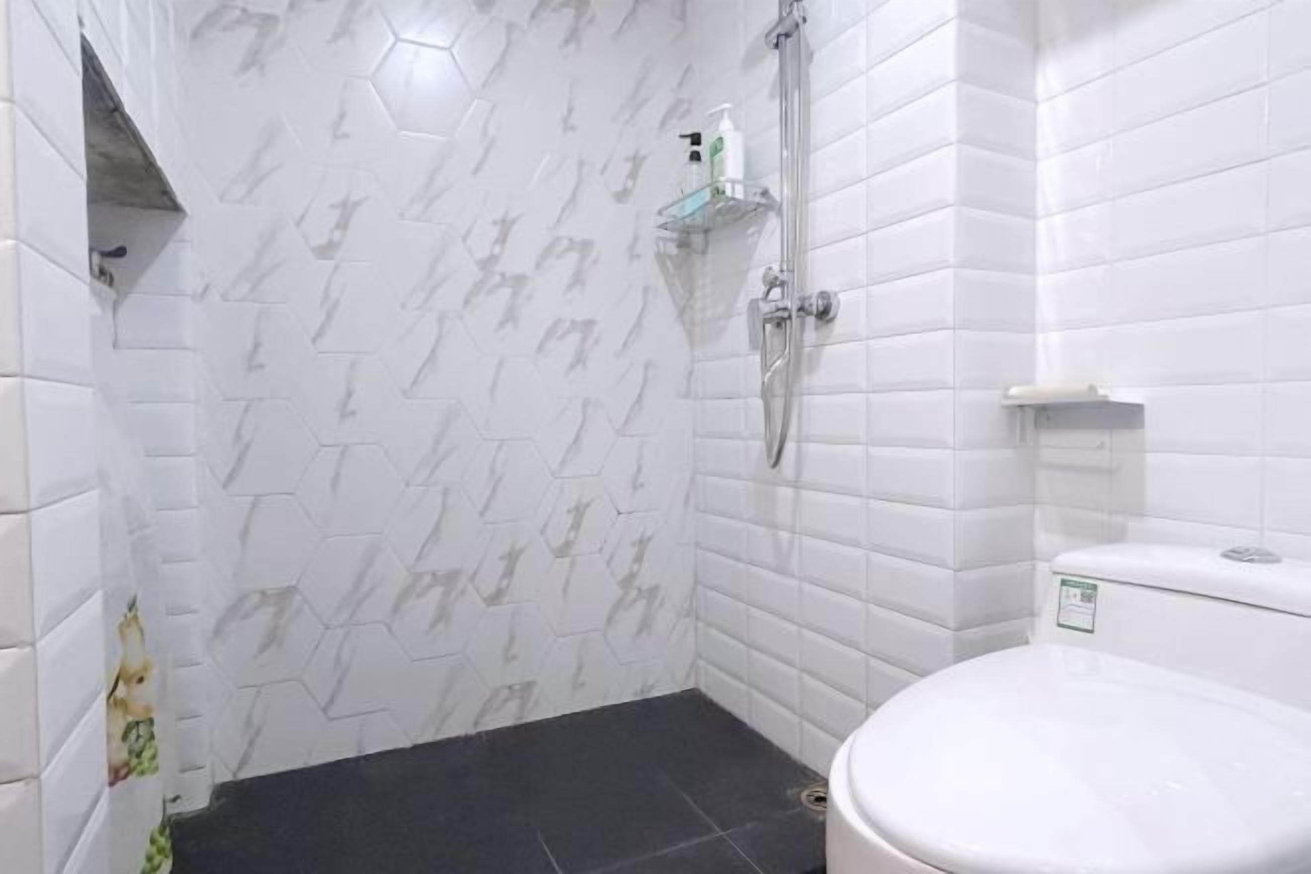 Kylpyhuone, jossa on valkoiset kuusikulmaiset laatat, suihku, wc ja hylly, jossa on hygieniatuotteita.