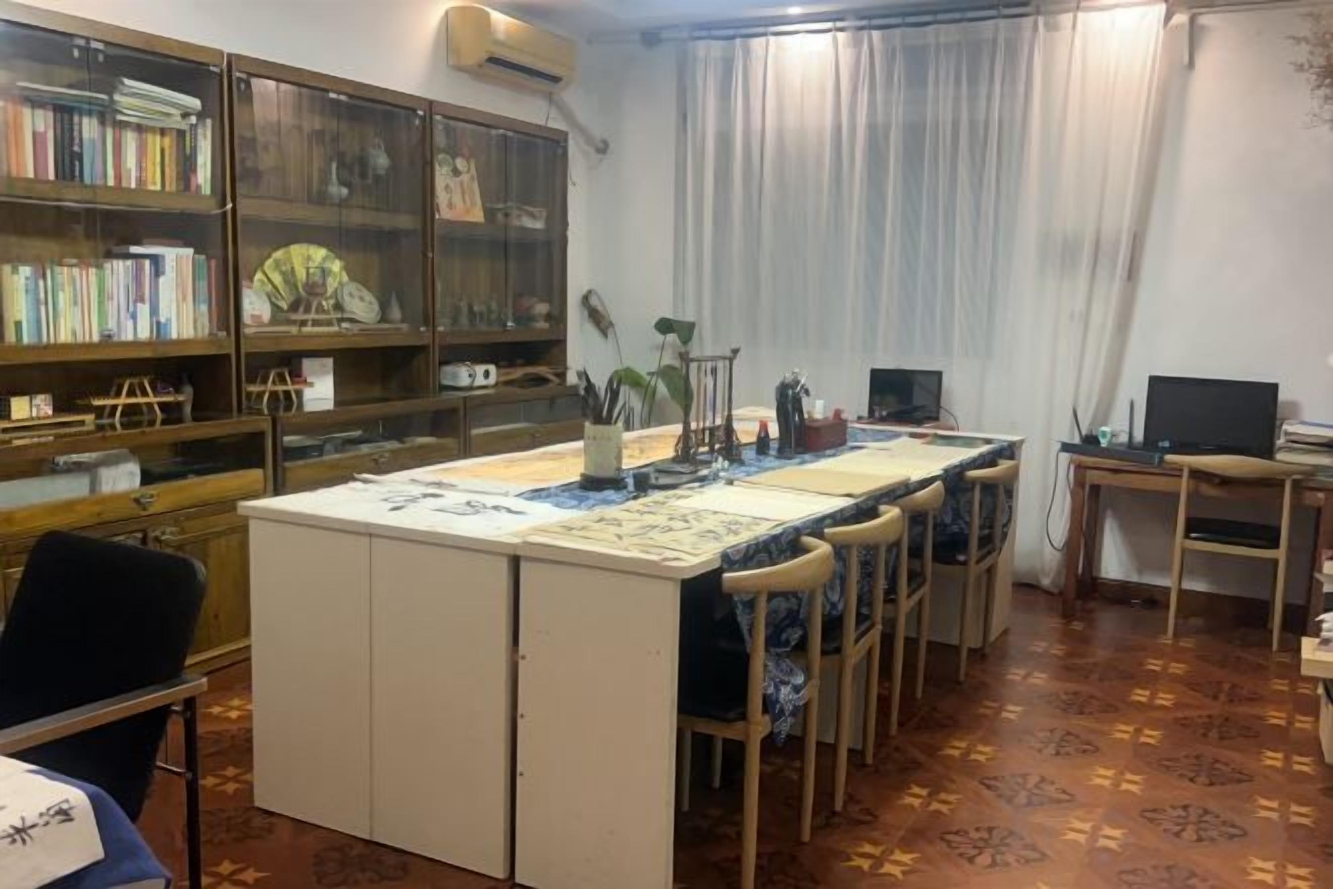 A room with a desk, chair, bookshelf, and a table with a laptop.