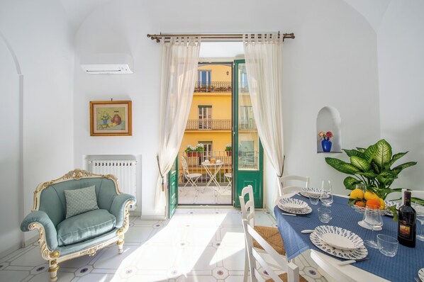 A dining area with a table set for two, a sofa, and a view of a balcony with a railing.
