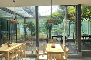 Un comedor interior con amplios ventanales, mesas de madera y lámparas colgantes.
