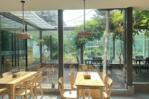 Un comedor interior con amplios ventanales, mesas de madera y lámparas colgantes.