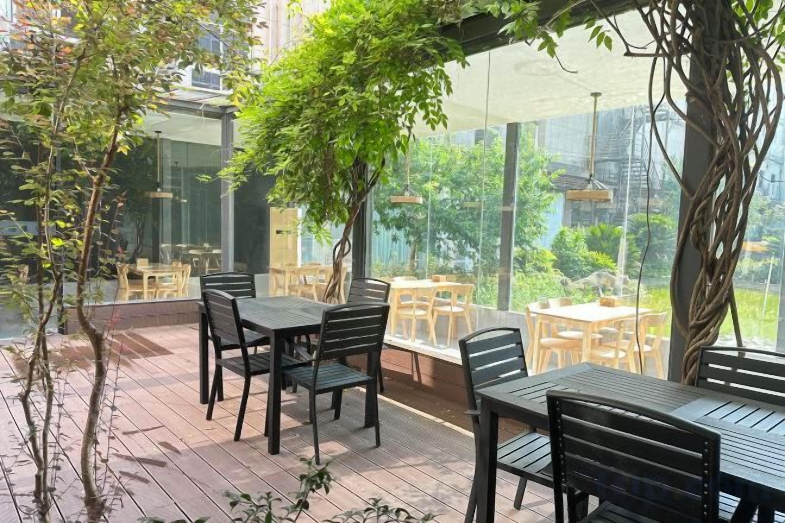 An outdoor patio with tables and chairs, surrounded by glass walls and greenery.